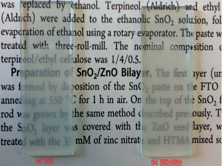 A imagem apresenta uma fotografia de um papel impresso com partes de um texto em inglês em fonte na cor preta. Sobre o papel há duas amostras: duas lâminas de vidro colocadas lado a lado, onde é possível observar que sua parte inferior, onde está localizada a amostra, o vidro fica com aspecto opaco, entretanto ainda é possível ver através deles parte do texto impresso no papel. Abaixo de cada uma das lâminas está escrito as indicações em fonte vermelha “(a) ZnO” e “(b) 50Zn50Sn”, da esquerda para a direita. Fim da descrição.